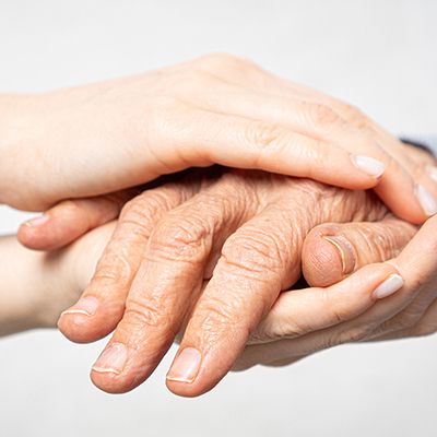 Eine junge Person hält die Hand einer älteren Person und zeigt damit Fürsorge und Unterstützung in einem Pflegekontext